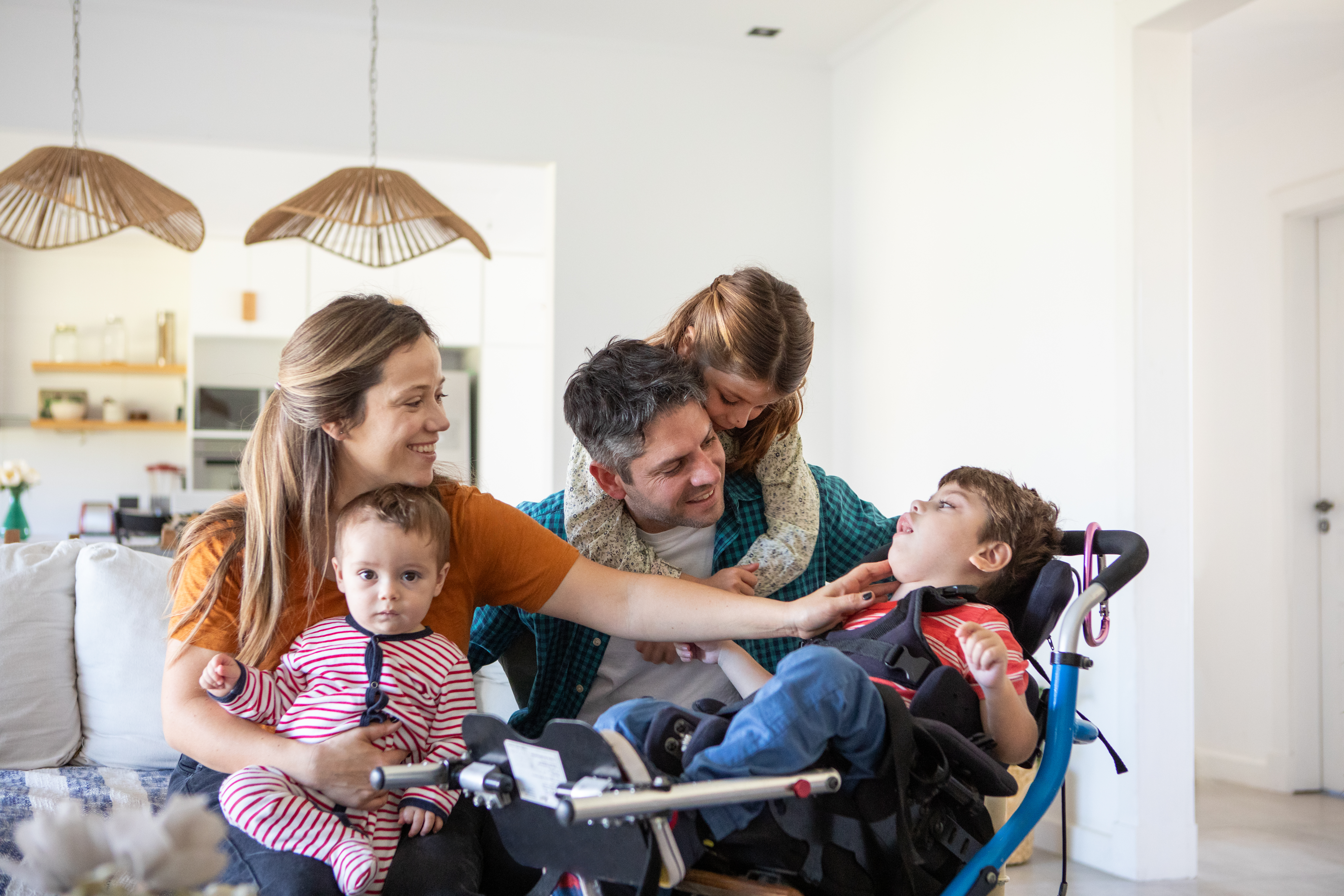 A mother and a father enjoy a moment at home with their 3 children, one of whom uses a tilt-in-space wheelchair