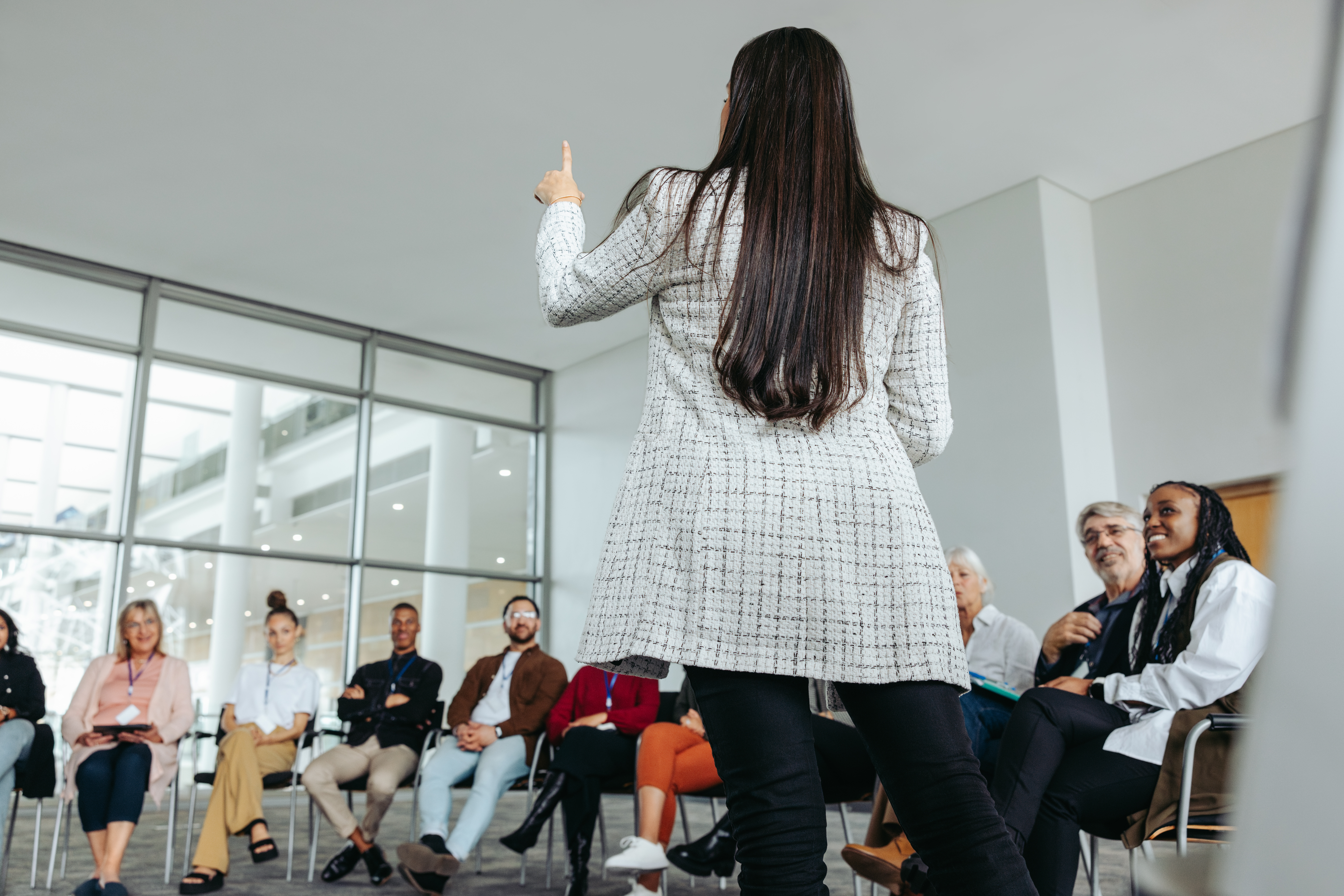 A woman in professional attire speaks to a small group of individuals at a business office